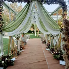 A breathtaking entrance for a day wedding, featuring a canopy of green and white drapes, crystal chandeliers, and floral arrangements.