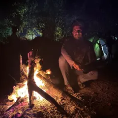 A trekker enjoying the warmth of a campfire. Our camping nights are filled with stories, music, and simple joys.