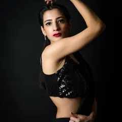 A dynamic portrait against a black background. The model's pose, with her arm raised, creates a strong line and adds movement to the shot, while the sequined top adds a touch of glamour.