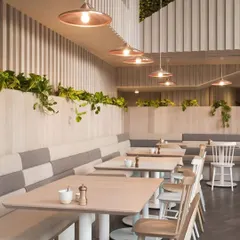 This cafe interior showcases a clean, minimalist aesthetic with a focus on natural light and textures. We used light wood for the paneling and tables, paired with custom two-tone upholstered bench seating and simple chairs to create a calm, relaxing environment perfect for a quiet coffee or meeting.