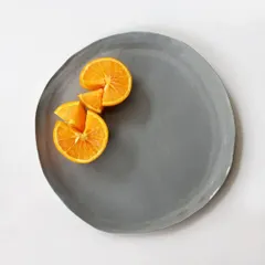 Our large monochrome grey dinner plate, shown here with fresh orange slices. The plate's organic, slightly irregular shape adds to its handmade charm and minimalist appeal.