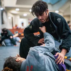 A student works to pass the guard of their training partner in a Gi. Our beginner classes focus on fundamental positions like this, building a strong base for your entire jiu-jitsu journey.