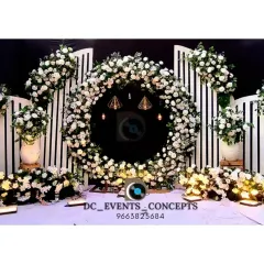 A chic and modern Mehendi backdrop featuring a circular wreath of white flowers against a clean, white slatted background. This minimalist design is perfect for a contemporary pre-wedding celebration.
