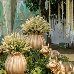 A close-up of the decor, featuring golden cow statues nestled in greenery, bunches of green bananas, and brass urns filled with tuberose, all elements of a traditional and prosperous celebration.