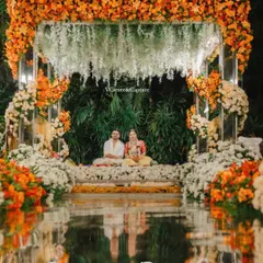 A breathtaking view of the couple seated in their magnificent floral mandap, reflected in the water below. This symmetrical and artistic shot highlights the grandeur of the decor and the serenity of the moment.