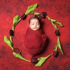Wrapped in love, surrounded by grace. This simple, elegant setup with a pop of red and a floral wreath beautifully frames this sleeping newborn.