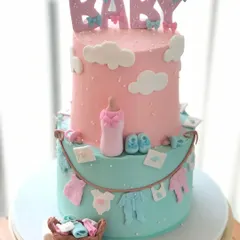 A classic two-tiered baby shower cake in pink and blue. It's decorated with a clothesline of baby items, a bottle, and booties.
