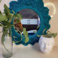 The finished green sunburst macrame mirror styled on a console table with plants. It adds a wonderful handmade touch and a splash of color to this serene corner.
