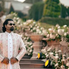 A full shot of the groom's outfit against the stunning backdrop of the wedding venue. This textured, off-white sherwani is a perfect example of modern royal wedding wear.