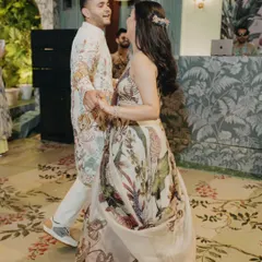 The couple shares their first dance at a tropical-themed welcome soiree. Their coordinated floral outfits perfectly match the lush, nature-inspired decor and custom-printed carpet.
