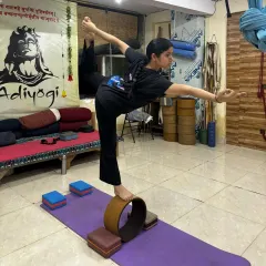 A student holds a challenging extended standing balance pose (Utthita Hasta Padangusthasana) on a yoga wheel. This builds leg strength, core stability, and focus.