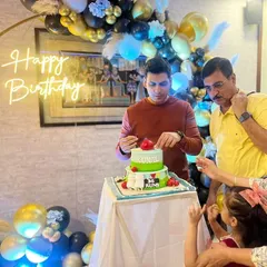 A family celebrating a birthday with a personalized cricket-themed cake as the centerpiece.