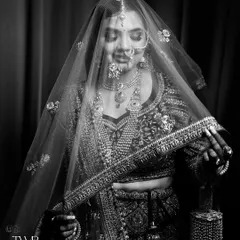 A beautiful black and white portrait of the bride looking down, her face partially covered by her veil. The focus on her intricate jewelry and serene expression creates a classic and elegant feel.
