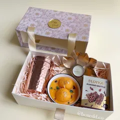 A beautiful Diwali gift box featuring a copper-hammered jar, a bowl of motichoor-inspired sweets, and almond brittle, presented with a drawer-style opening.