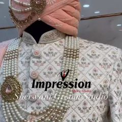 The classic white and peach combination is timeless. This intricately embroidered white sherwani, paired with a delicate peach pagdi and a multi-layered pearl mala, is designed to perfectly complement the bride's attire.