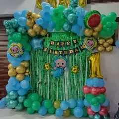 A vibrant Cocomelon theme for a first birthday. This decoration includes a green tinsel backdrop, a colorful balloon frame with gold accents, and a large number '1' foil balloon.