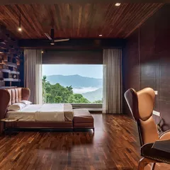 The master bedroom in the Chikmagalur residence, where a feature wall of stacked wooden blocks adds texture and warmth. A large window frames the mountain view, making it the primary artwork in the room.