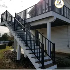 This sturdy, straight outdoor staircase provides safe and reliable access to an elevated deck. The black metal railing with vertical balusters offers a classic look that complements the home's traditional siding.