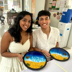 A happy couple showing off the beautiful resin beach art they created together. It's a perfect activity for a creative date, and you both get to take home a piece of the ocean.