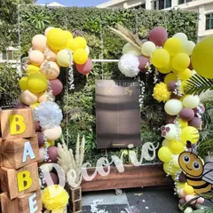 A full view of an outdoor "What will it Bee?" gender reveal party. I used a green wall as a natural backdrop, adding wooden 'BABEE' blocks, a cute bee cutout, and a balloon garland in yellow, maroon, and beige.