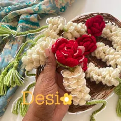 A close-up of my desi-inspired crochet gajra. I use off-white yarn to mimic mogra flowers and add pops of red with tiny roses, all held together with green yarn tassels.