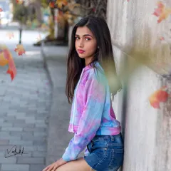 A subtle and stylish street portrait with a touch of autumn feeling from the falling leaves effect. The model's casual pose and tie-dye hoodie create a simple, relatable, and fashionable image.