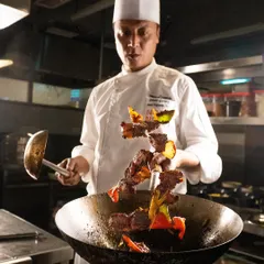 A chef tossing meat and vegetables. This behind-the-scenes action shot tells a story of freshness and expert preparation.