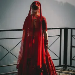 A bridal portrait that emphasizes the scale of the landscape. The bride in her traditional red lehenga, looking out at the mountains, creates a powerful and poetic image.