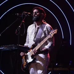 The bassist of Sanam Band entertains the crowd during a live Sangeet performance, set against a backdrop of neon circles.