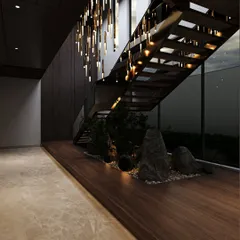 This design concept for an upcoming residence features a zen-like garden beneath a modern staircase. The combination of natural rocks, pebbles, and carefully selected plants, illuminated by a dramatic chandelier, creates a serene and artistic statement.
