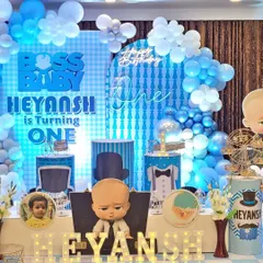 A fun and stylish Boss Baby themed birthday stage. The setup includes a custom light-up backdrop, character cutouts, themed pedestals for the cake, and marquee letters spelling out the birthday boy's name.