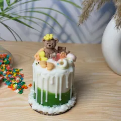 A close-up shot of my signature teddy bear cake candle. The green base, white drip effect, and adorable toppings make it a whimsical and sweet centerpiece or gift for any baby shower.