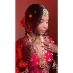 A profile shot capturing the intricate details of the hair and makeup. The soft curls and fresh flowers in her bun complement the timeless beauty of her red bridal attire.
