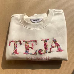This custom sweatshirt features the name 'TEJA' embroidered with a dense floral pattern, with a special date stitched below. A beautiful anniversary or birthday gift.