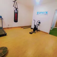 This is our dedicated fitness area, equipped specifically for shooters. You can see the treadmill for endurance, a punching bag for power, an exercise bike for cardio, and a balance board in the foreground, a key tool we use for stability training.