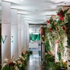 A beautifully designed walkway leading to the main event space. The path is lined with white and red flowers, and one side features panels telling the couple's love story, creating a personal and meaningful journey for the guests.