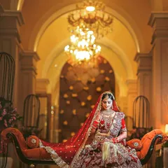 An elegant bride seated in a luxurious, warmly lit hall, looking like royalty in her elaborate wedding dress.