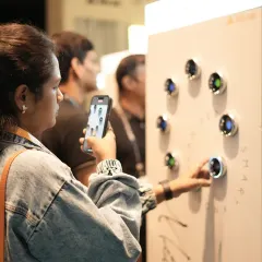A visitor uses her phone to capture an interactive display of colorful smart buttons, showcasing how our expo allows for personal evaluation and content creation.