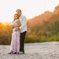 A warm embrace on the sandy riverbank as the sun sets behind the hills. The golden light creates a beautiful, soft glow, making this a deeply romantic and serene portrait.