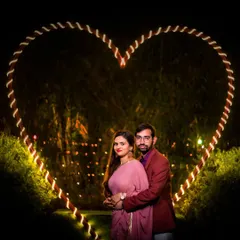 A classic romantic portrait framed by a large, illuminated heart. This is a popular and beautiful setup for nighttime pre-wedding photography.