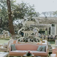 Elegant seating for a garden party, featuring a vintage pink sofa and a three-tiered floral fountain. We mix different furniture styles to create visual interest and comfortable lounging areas.