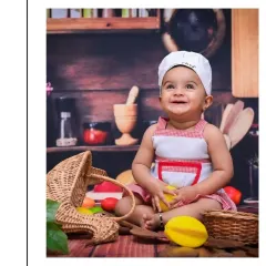 A joyful shot from a 'Little Chef' setup. Dressed in a chef's hat and apron, this baby is surrounded by kitchen-themed props, creating a fun and imaginative scene.