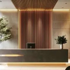 A striking reception area with a minimalist dark stone desk, accented by warm lighting from below. The back wall features dramatic copper-toned fluted panels, creating a luxurious and memorable first impression.