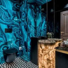 A powder room that makes a bold statement. The walls are clad in a vibrant blue malachite-patterned tile, contrasted by a striking illuminated quartz pedestal sink. The geometric black and white flooring adds another layer of graphic drama.