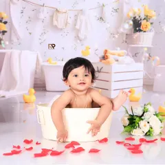 A joyful baby boy splashes happily in a tub filled with flowers and bubbles. The bright, clean background and colorful lanterns make this a cheerful and vibrant portrait.