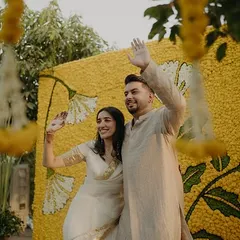 The couple waving against a vibrant marigold backdrop, their coordinated neutral outfits creating a calm and elegant picture.