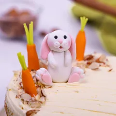 A close-up of the adorable, hand-crafted bunny topper, nestled among fondant carrots and nuts.