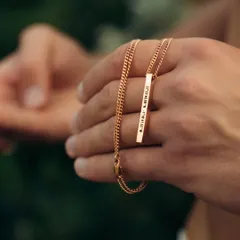 A hand holding a rose gold bar pendant engraved with coordinates. This shot highlights the warm tone of the rose gold finish and the precision of the custom engraving.