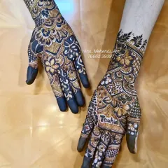 The beautiful contrast of a dark henna stain. The design features bold flowers and the name 'Tauhid' on the palm.