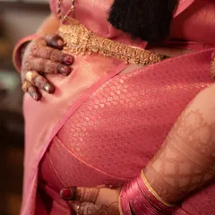 This detail-oriented shot focuses on the mother-to-be's hands, decorated with henna, cradling her baby bump. The vibrant pink saree and traditional gold jewelry highlight the cultural beauty of the ceremony.